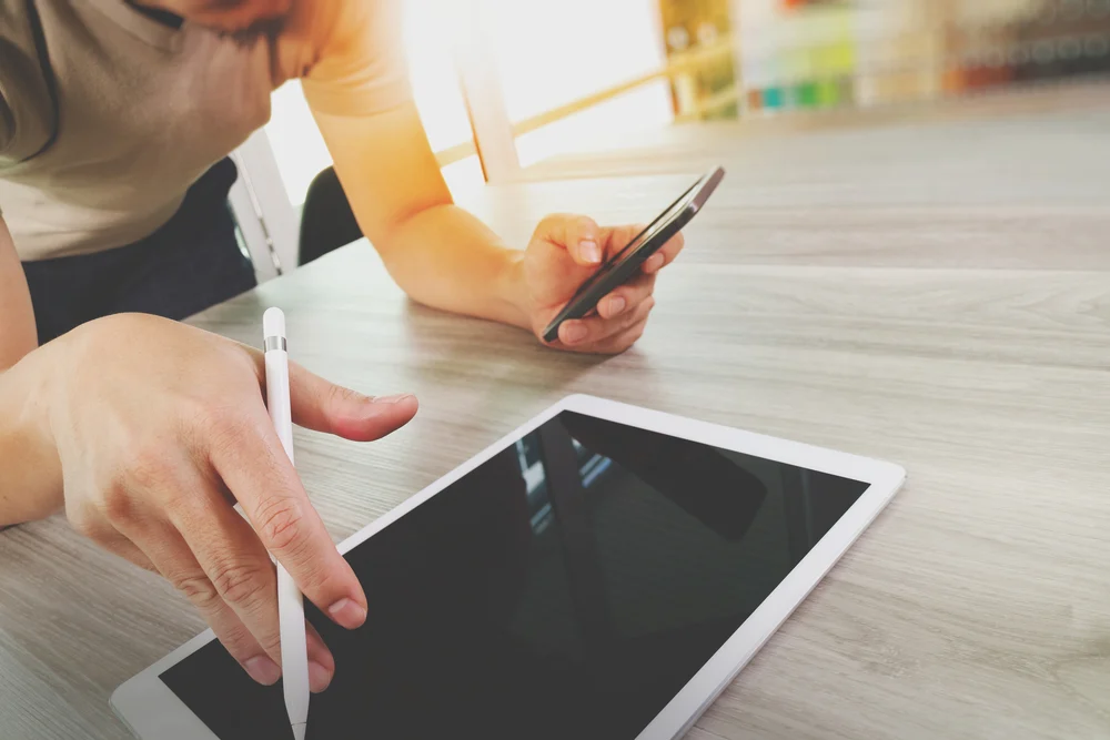top-view-of-Designer-hand-working-with-digital-tablet-computer-and-smart-phone-on-wooden-desk-as-responsive-web-design-concept